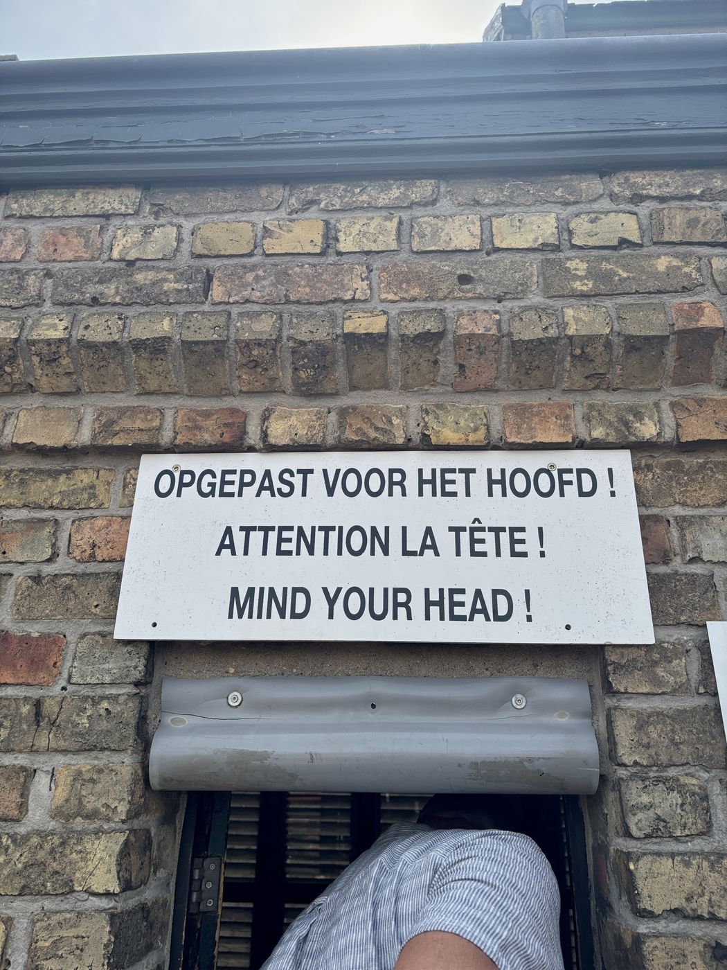 A “mind your head” sign over a very low brick doorway
