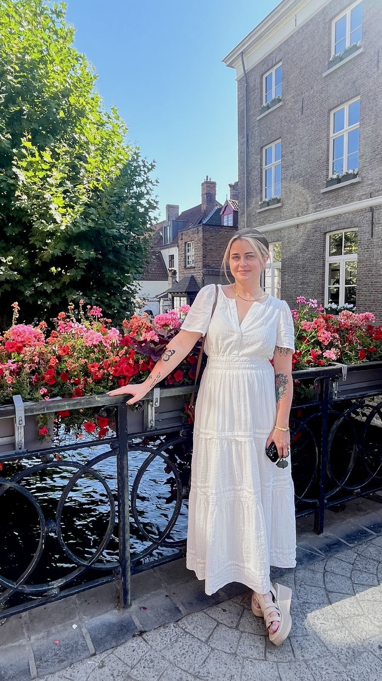 Me in a white dress on a flower-lined bridge in Bruges